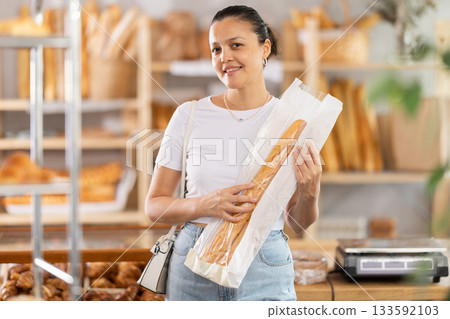Asian woman buyer with baguettes in plastic package stands in trading floor of bakery Asian woman buyer with baguettes in plastic package stands in trading floor of bakery 133592103