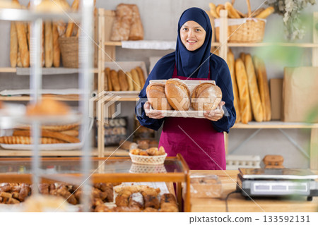 Asian Muslim woman bakery worker sells bread, stand at counter and wait for visitors Asian Muslim woman bakery worker sells bread, stand at counter and wait for visitors 133592131