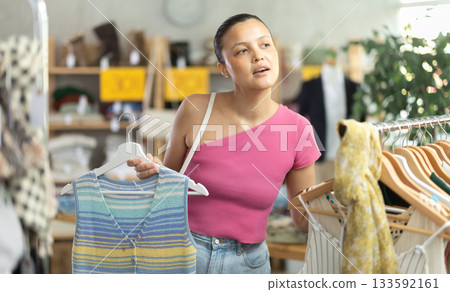 Attentive young Asian woman choosing something for summer in clothing store 133592161