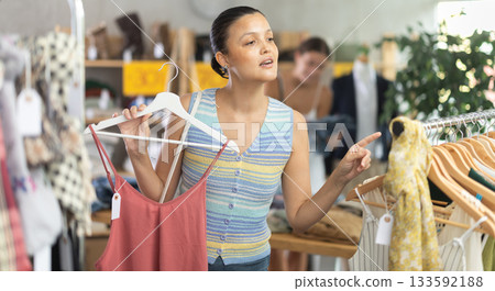 Near rack, asian woman buy summer clothes, choose some items. Female client looking for something in background 133592188