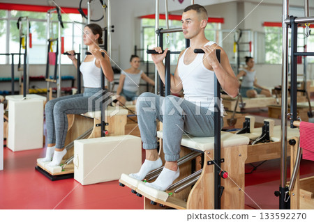Young guy training her legs in seated position on combo chair Young guy training her legs in seated position on combo chair 133592270