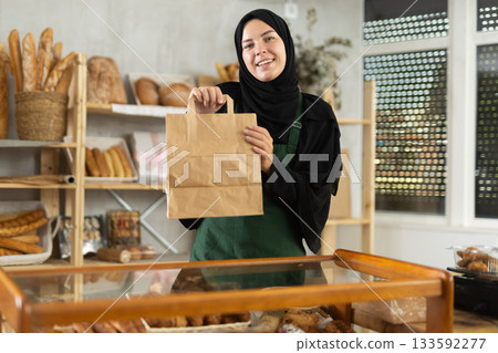 Saleswoman in hijab holding paper bag in bakery 133592277