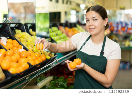 Female seller in apron chooses juicy tangerine Female seller in apron chooses juicy tangerine 133592289