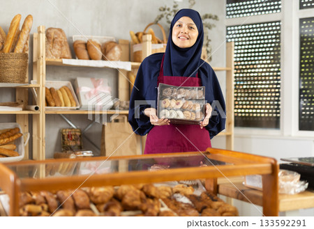Middle-aged Muslim saleswoman holds cookie box in bakery Middle-aged Muslim saleswoman holds cookie box in bakery 133592291