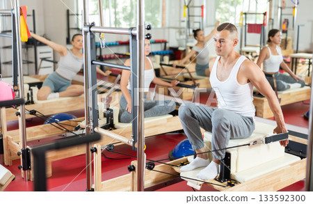 Young guy doing arm exercises on cable reformer device Young guy doing arm exercises on cable reformer device 133592300