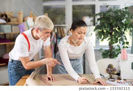 Female and male dressmakers drawing on paper in sewing studio 133592313