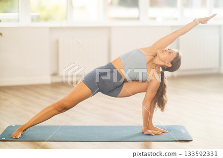 Lover of active lifestyle on yoga mat perform doing elongated side angle in gym Lover of active lifestyle on yoga mat perform doing elongated side angle in gym 133592331