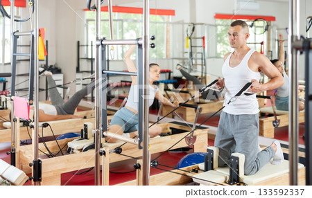 Young guy doing arm exercises on cable reformer device 133592337