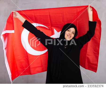 Young Muslim woman in black hijab holds unfurled flag of Turkey. 133592374