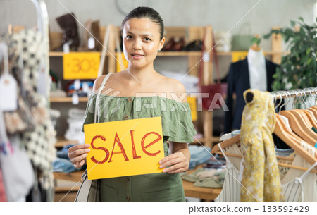 Asian woman with poster in her hands announces clothing discounts 133592429