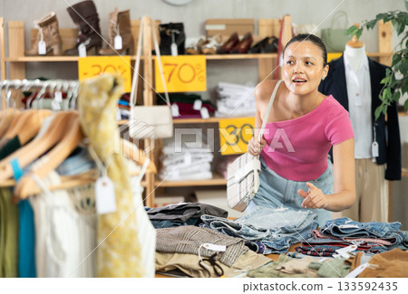 Young woman chooses fashionable jeans or shorts in clothing store for summer season 133592435