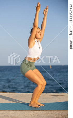 Athletic girl meditates in a yoga pose parshvottanasana on seashore 133592458