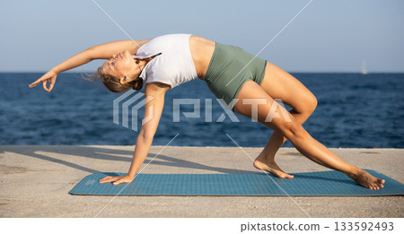 Sportive girl practicing wild thing pose of yoga on seashore Sportive girl practicing wild thing pose of yoga on seashore 133592493