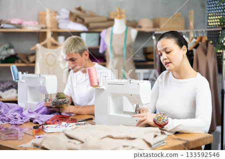 Male and female dressmakers working with sewing-machine in tailor's workshop Male and female dressmakers working with sewing-machine in tailor's workshop 133592546