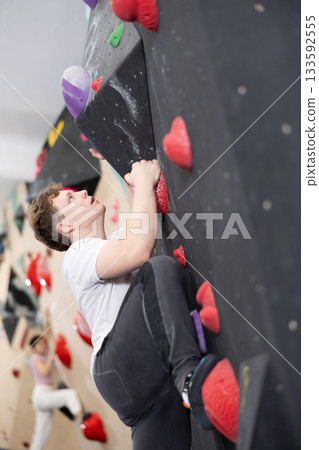 Teenage boy climbs steep artificial wall in sports complex and trains endurance Teenage boy climbs steep artificial wall in sports complex and trains endurance 133592555