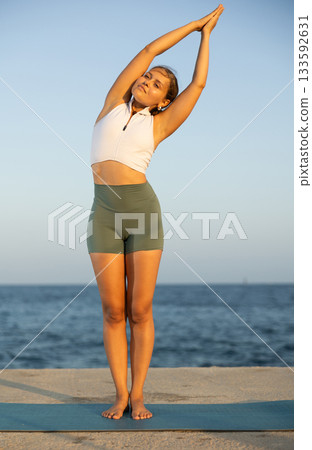 On windy day young slender woman does yoga near sea doing Vrikshasana On windy day young slender woman does yoga near sea doing Vrikshasana 133592631