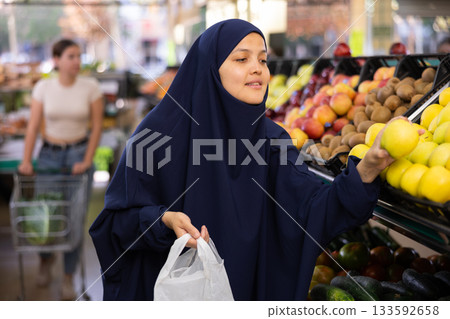 Young asian woman in hijab chooses quality juicy ripe apples Young asian woman in hijab chooses quality juicy ripe apples 133592658