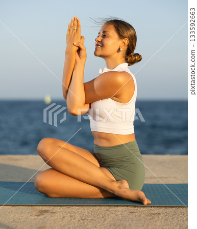 Relaxed girl performing Ardha Matsyendrasana position yoga training on beach Relaxed girl performing Ardha Matsyendrasana position yoga training on beach 133592663