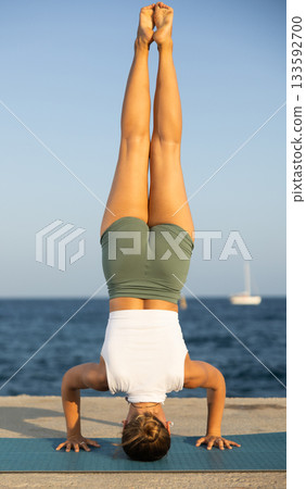 On windy day young slender woman does yoga near sea doing shirshasana On windy day young slender woman does yoga near sea doing shirshasana 133592700