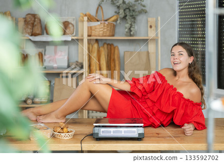 Woman in red dress sitting on counter in bakery 133592702