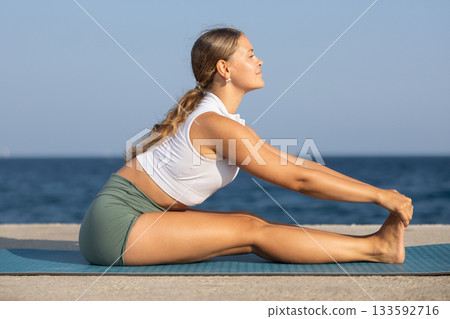 On windy day young slender woman does yoga near sea doing Pashchimottanasana On windy day young slender woman does yoga near sea doing Pashchimottanasana 133592716