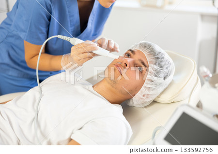 Young woman cosmetologist doing exfoliation to young man Young woman cosmetologist doing exfoliation to young man 133592756