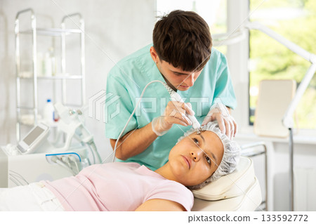 Young male cosmetologist doing microcurrent procedure to young woman 133592772