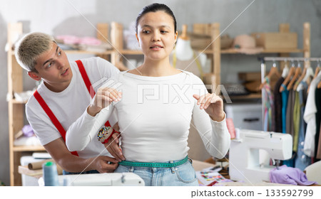 Professional qualified male dressmaker taking measurements of woman client for tailoring in sewing workshop 133592799