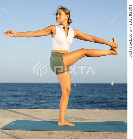 Athletic girl meditates in a yoga pose parshvottanasana on seashore 133592801