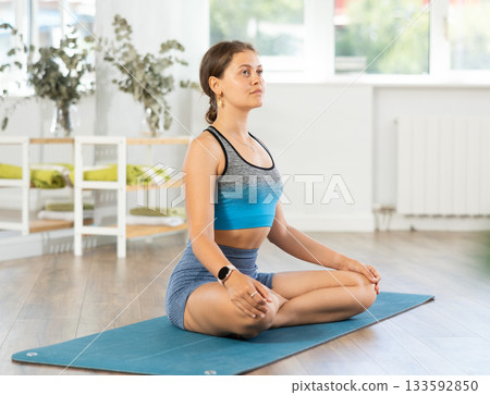 Lover of active lifestyle on yoga mat perform doing variations of padmasan in gym Lover of active lifestyle on yoga mat perform doing variations of padmasan in gym 133592850