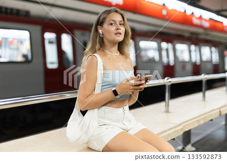 Woman sitting at metro station with headphones and phone Woman sitting at metro station with headphones and phone 133592873