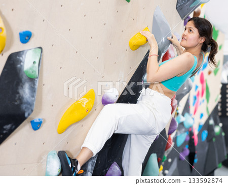 Young Asian woman climbs steep artificial wall in sports complex and trains endurance Young Asian woman climbs steep artificial wall in sports complex and trains endurance 133592874