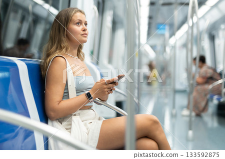 Young woman sitting in subway car with phone Young woman sitting in subway car with phone 133592875