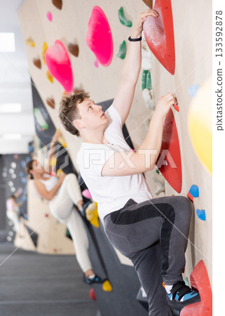 Teen guy practicing rock climbing on climbing wall 133592878