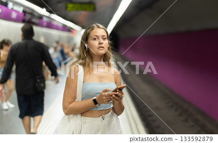 Woman in headphones with phone stands at metro station 133592879