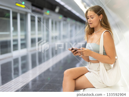 Young girl sitting in subway platform holding phone in hand 133592904