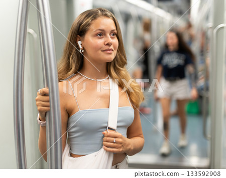 Young woman is standing in subway car with headphones 133592908