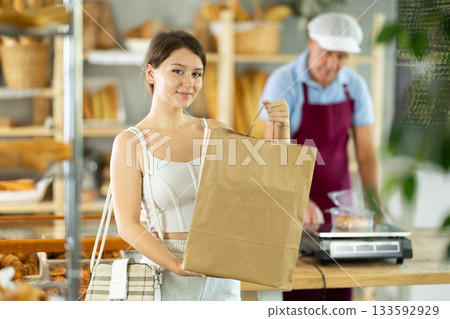 Portrait of young girl buyer with paper bag of fresh baked goods in interior of bakery 133592929