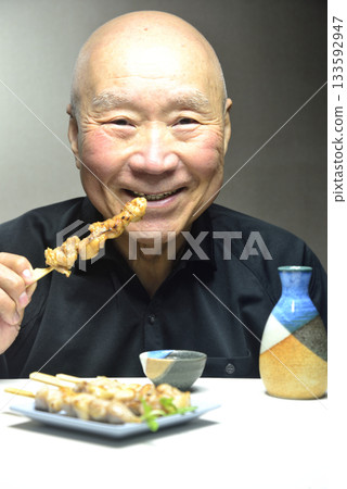 Smiling old man eating yakitori and drinking sake 133592947