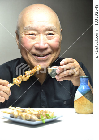 Smiling old man eating yakitori and drinking sake Smiling old man eating yakitori and drinking sake 133592948
