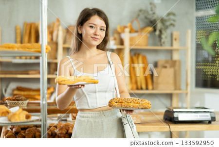 Young female customer stands with bocadillo in hands near window of bakery. Young female customer stands with bocadillo in hands near window of bakery. 133592950