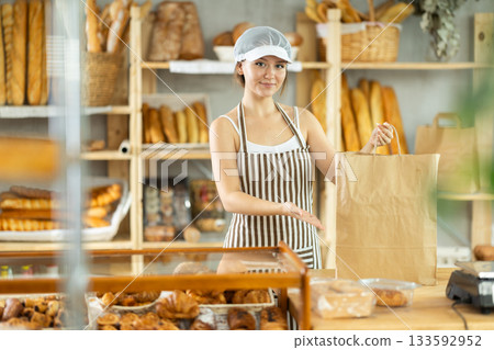 Girl entrepreneur owner of bakery holds out paper bag with pastries in hand Girl entrepreneur owner of bakery holds out paper bag with pastries in hand 133592952