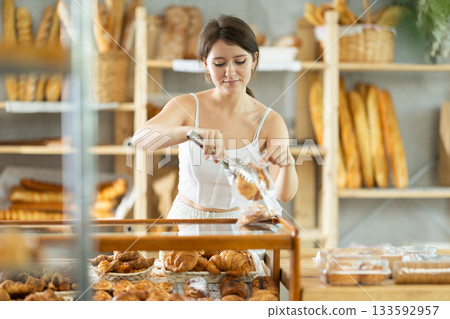 European young woman visitor puts croissant in plastic disposable bag European young woman visitor puts croissant in plastic disposable bag 133592957