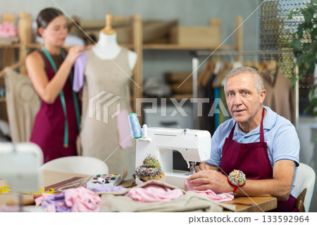 Elderly man sews on machine female assistant sews on mannequin Elderly man sews on machine female assistant sews on mannequin 133592964