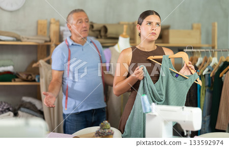 Elderly man scolding young woman in sewing workshop Elderly man scolding young woman in sewing workshop 133592974