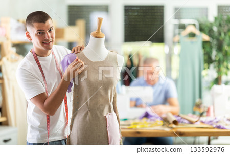 Young man working with mannequin, elderly man sewing Young man working with mannequin, elderly man sewing 133592976