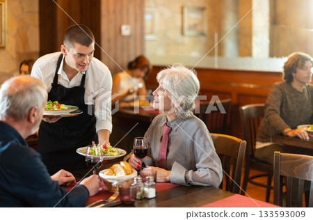 Waiter brings order to elderly man and woman couple 133593009