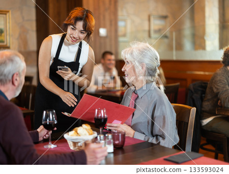 At cafe, Filipino girl waitress communicates with mature couple of customer, accepts order At cafe, Filipino girl waitress communicates with mature couple of customer, accepts order 133593024