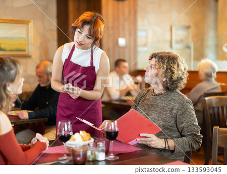 At cafe, Filipino girl waitress communicates with man and mature woman customer, accepts order 133593045
