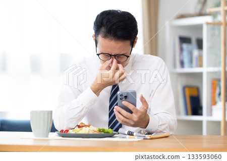 一名男子在上班前一邊吃飯一邊看手機。 一名男子在上班前一邊吃飯一邊看手機。 133593060